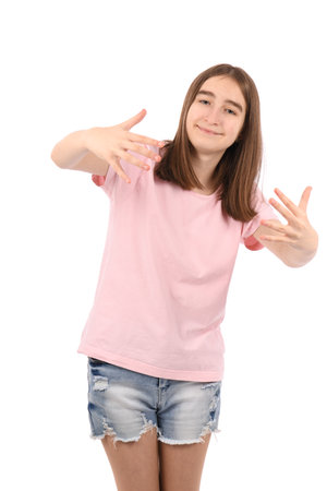 Young beautiful girl in a pink t-shirt and denim shorts on a white background, smiling at the camera and hugging with both hands.の写真素材