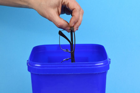 Hand holding plastic black glasses and puts in blue container, isolated on white background. High resolution photo. Full depth of field.の写真素材
