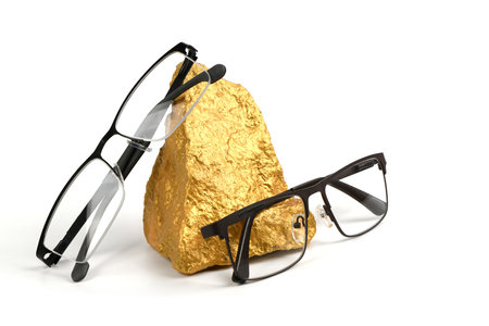 Pair of reading glasses on golden shining nuggets isolated on white background. High resolution photo. Full depth of field.の写真素材