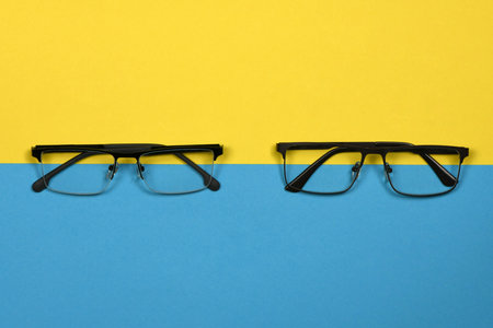 Pair of reading glasses isolated on blue and yellow background. Fashion performances for man and woman. High resolution photo. Full depth of field.の写真素材