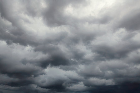 Dark dramatic sky with black stormy clouds before rain or snow as abstract background, extreme weather, the sun shines through the clouds, high contrast photo.の写真素材