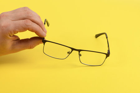 Hand holding plastic black glasses, isolated on yellow background. High resolution photo. Full depth of field.の写真素材