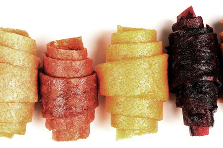 Candy pastila. A line of four assorted fruit leather rolls standing upright on a white background. A...