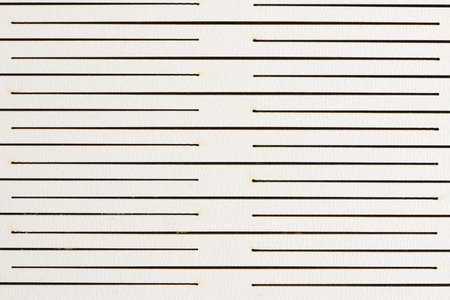 Full-frame, close-up view of a white or light beige paper or board surface featuring a pattern of thin, black, interrupted horizontal lines or slots, creating a rhythmic texture.の写真素材
