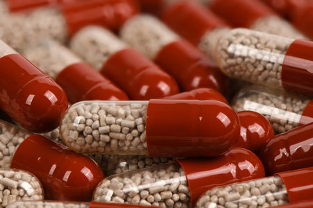 Close-up of medical capsules with red caps and clear bodies containing sustained-release pellets....