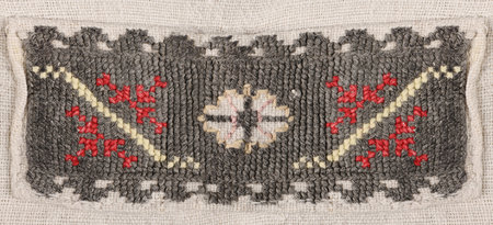 Macro detail of thick dark gray woven fabric decorated with red and white geometric embroidery...
