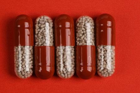 Macro shot of five pharmaceutical hard gelatin capsules with red caps and clear bodies containing...