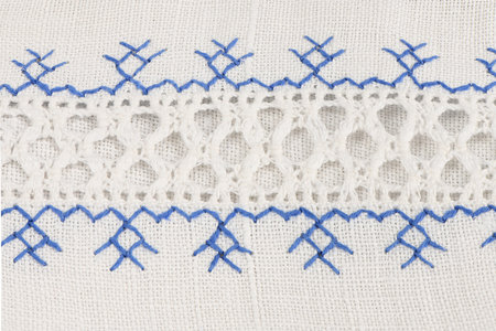 Close-up texture of handmade textile showing white lace openwork and blue geometric embroidery...