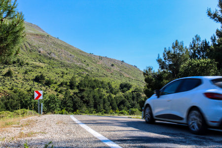 Car on asphalt island road, about to cornering. Road lined with trees and mountains around.