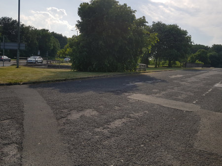 Sunlit view of a side road in a state of disrepair next to the main road lined with trees and foliage on a bright summer day.の写真素材