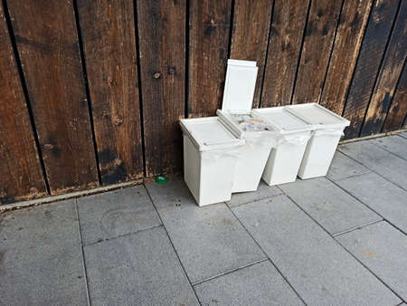 four white filled garbage cans in front of a wooden facadeの写真素材