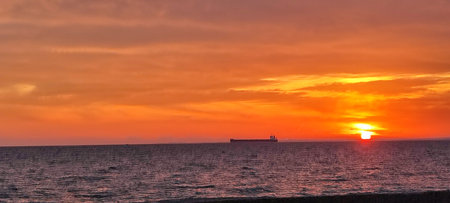 Sunset over the sea with a cargo ship in the foreground.の写真素材