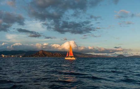 Beautiful sunset vista with a sailboat in the foreground off the coast of Honolulu on Oahu, Hawaiiの写真素材