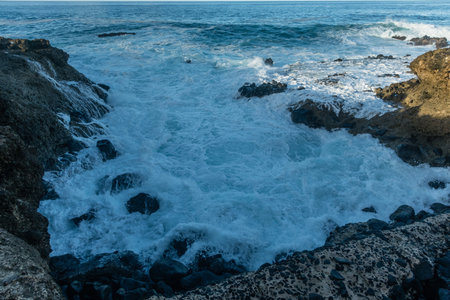 Scenic vista of waves breaking against the rocky shore in a small cove along the Kaena Point trail on Oahu, Hawaiiの写真素材