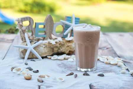 Glass of frozen coffee on wooden table with sand, shells, rocks and starfish.の写真素材