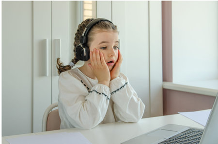 Cute little shocked girl studying on the computer at home. Back to school. Online school.
