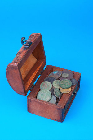 Wooden chest with coins inside isolated on blueの写真素材