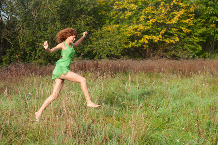 Young beautiful sexy girl in a green dress runs on a gladeの写真素材