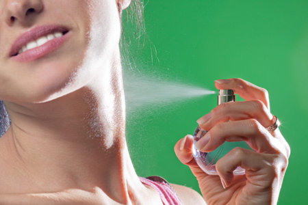 Beautiful young woman spraying parfume on green background
