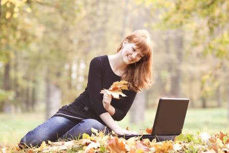 The beautiful girl in autumn park with the laptopの写真素材