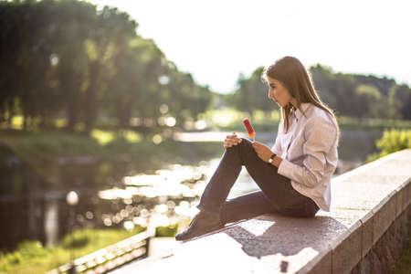 Beautiful young brunette girl sitting outdoors near the riverの写真素材