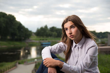 Beautiful young brunette girl sitting outdoors near the riverの写真素材
