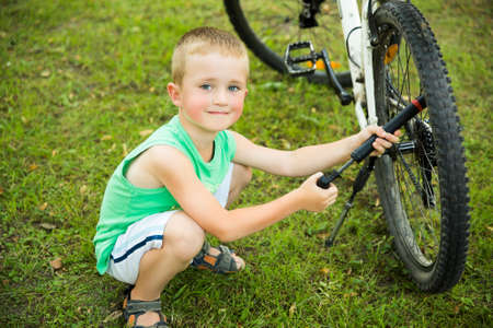 Young boy pumping thÑ bicycle tube on meadowの写真素材