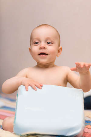 Baby with package of diapers sitting on sofaの写真素材