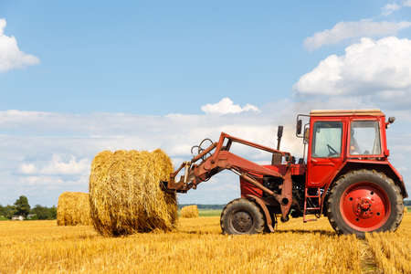 Tractor carrying hay at field in summer dayの写真素材
