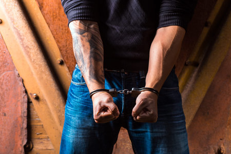 Tattooed hands of a criminal handcuffed. Rear view.