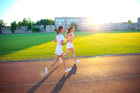 GRODNO, BELARUS - JUNE 17, 2013: beautiful young women exercise jogging and running on athletic track on stadium at sunriseのeditorial素材
