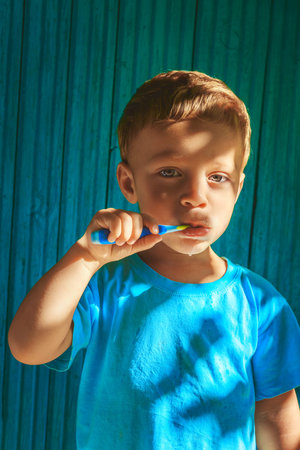 Boy cleaning teeth on wooden blue background