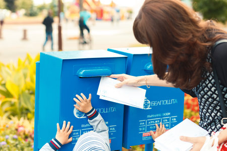 Kids helps her mother to puts letters in the mailbox to send