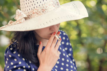 Woman in a hat smoking a cigarette in a gardenの写真素材
