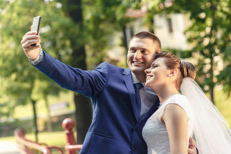 bride and groom make selfi on the summer park backgroundの写真素材