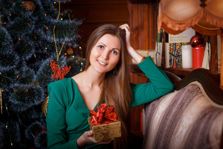 Beautiful woman with cristmas gift sitting on armchair at home