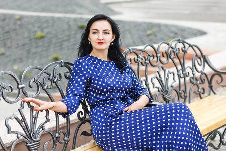 beautiful young brunette woman in blue dress sitting on a benchの写真素材