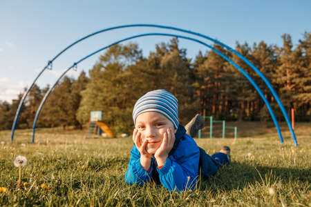 Little boy warmly dressed lying on a green grassの写真素材