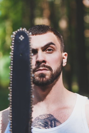 portrait of aggressive muscular male lumberjack, woodworker with chainsaw in hand, posingの写真素材