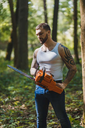 portrait of aggressive muscular male lumberjack, woodworker with chainsaw in hand, posingの写真素材