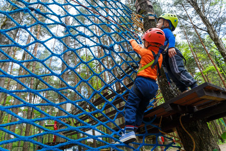 Twin bothers climbing in adventure park is a place which can contain a wide variety of elements, such as rope climbing exercises, obstacle courses and zip-lines.の写真素材