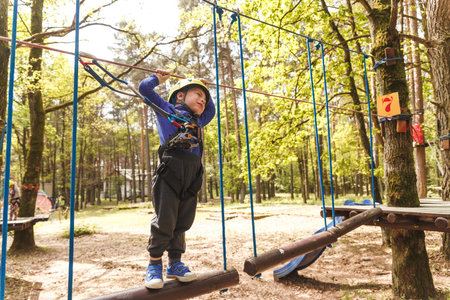 Young boy in helmet walks by pendant tree log at sunny summer day in adventure playground
