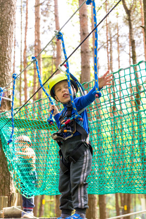 Young boy in helmet walks by rope at sunny summer day in adventure playground