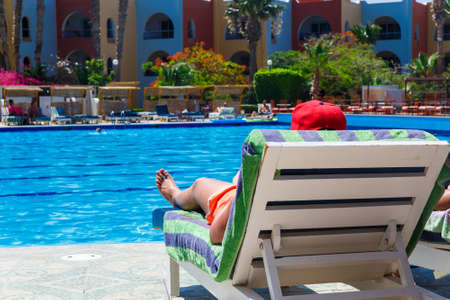 Sunbathing by the hotel tourist resort swimming pool, man lying down on a sunlounger looking over the waterの写真素材