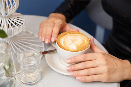 Close-up female hands holding cup with coffee cappuccino with foam with pattern heart. Perfect...