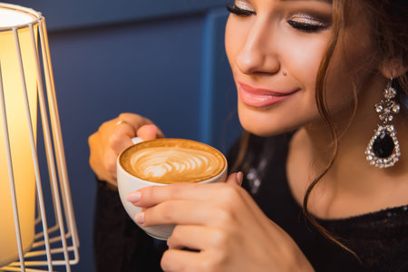 Close up of young beautiful woman hands holding hot cup of cappuccino coffee