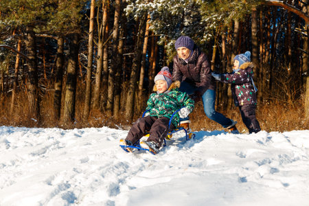 Happy young woman with two children on a sled on winter walk