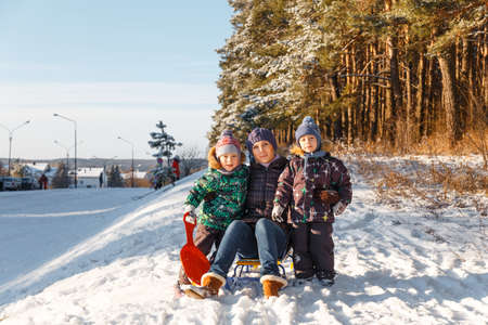 Happy young woman with two children on a sled on winter walkの写真素材