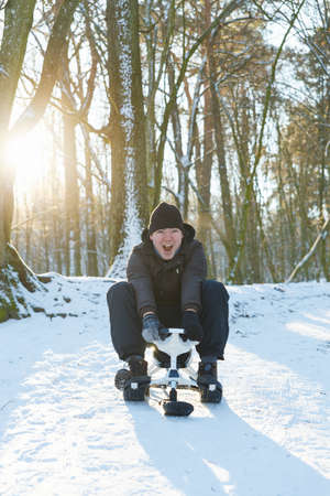 Young man riding a snow scooter from the mountain at sunny frosty dayの写真素材