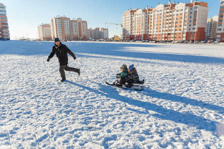 Father and two sons sledding in winter area in cityの写真素材